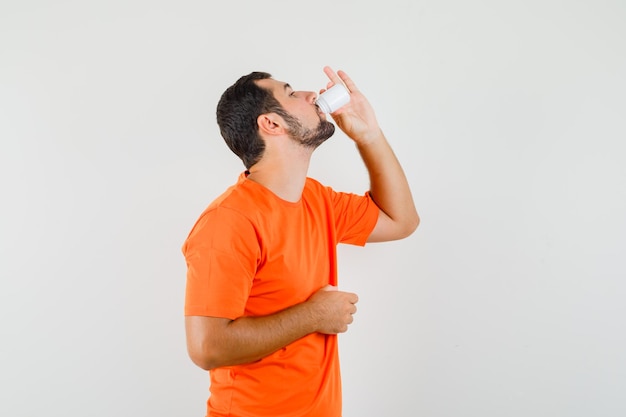 Hombre joven en camiseta naranja tomando pastillas, vista frontal.