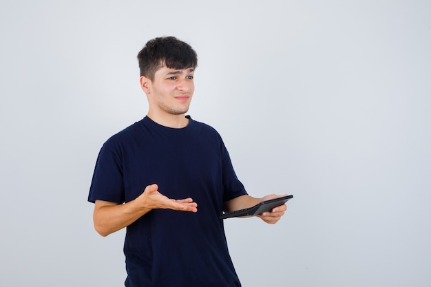 Hombre joven en camiseta negra con calculadora y mirando decepcionado, vista frontal.