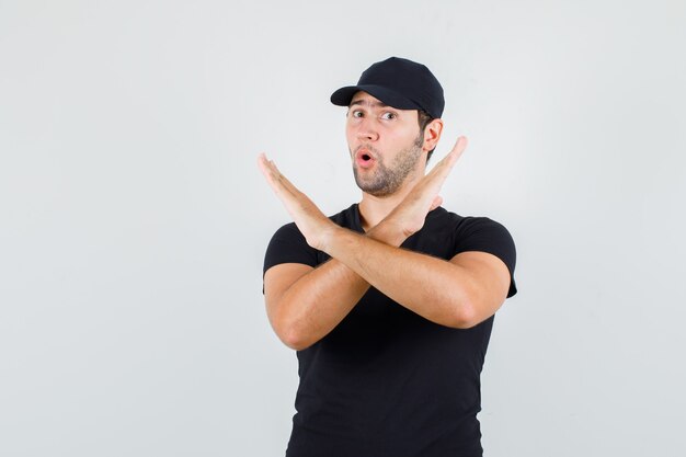 Hombre joven en camiseta negra, gorra mostrando gesto de parada y mirando emocionado