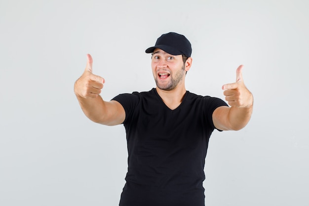 Hombre joven en camiseta negra, gorra mostrando gesto de pistola y mirando alegre