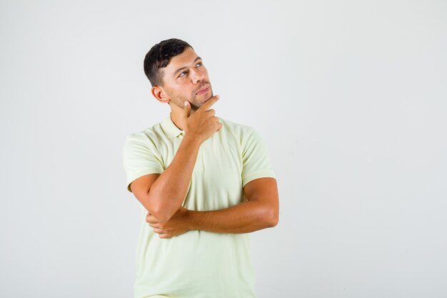 Hombre joven en camiseta poniendo el dedo en la barbilla y mirando pensativo