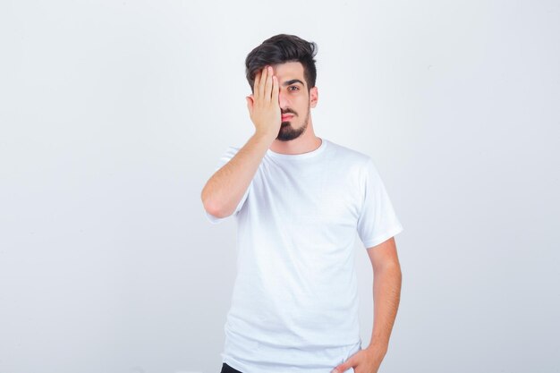 Hombre joven en camiseta que cubre los ojos con la mano y parece seguro