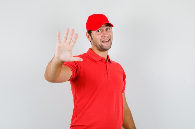 Hombre joven en camiseta roja, gorra mostrando gesto de rechazo cortésmente
