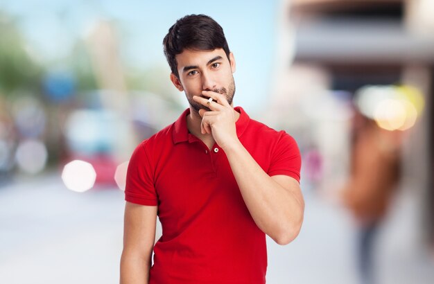 Hombre joven con camiseta roja sujetando un cigarro