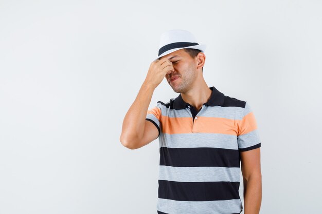 Hombre joven en camiseta y sombrero frotándose los ojos y mirando con exceso de trabajo