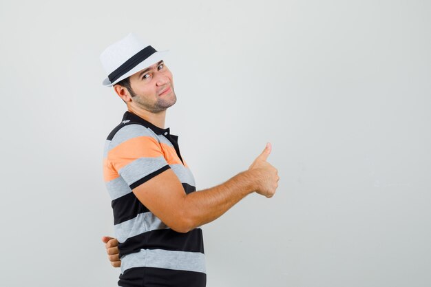 Hombre joven en camiseta, sombrero mirando a un lado mientras muestra el pulgar hacia arriba y parece complacido