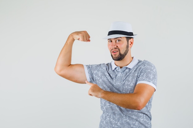 Foto gratuita hombre joven en camiseta, sombrero mostrando el músculo del brazo y mirando intrépido, vista frontal.