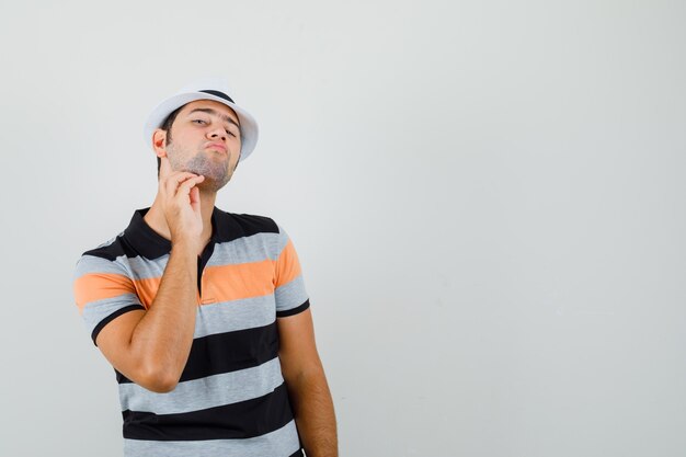 Hombre joven en camiseta, sombrero rascándose la barba y buscando espacio tranquilo para texto