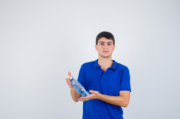 Hombre joven en camiseta sosteniendo una botella de plástico en las manos y mirando confiado, vista frontal.