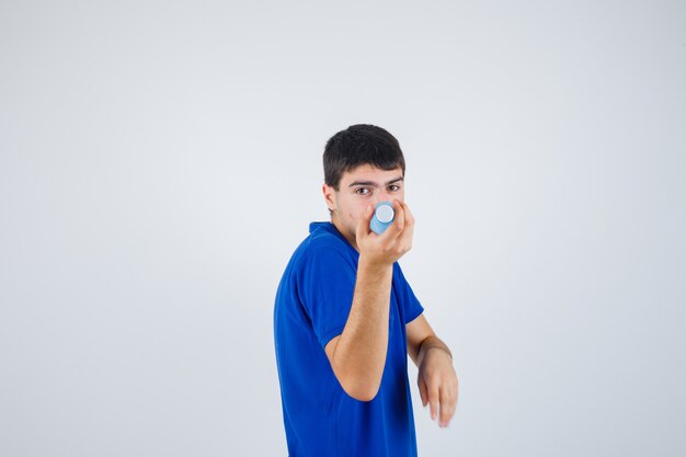 Hombre joven en camiseta sosteniendo una botella de plástico y mirando confiado, vista frontal.