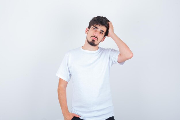 Hombre joven en camiseta sosteniendo la mano en la cabeza y mirando pensativo