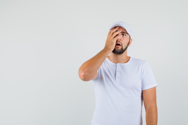 Hombre joven en camiseta sosteniendo la mano en su rostro y mirando asustado, vista frontal. espacio para texto