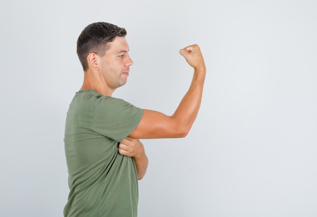 Foto gratuita hombre joven en camiseta verde militar que muestra músculos y parece fuerte.