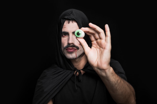 Hombre joven en capote negro con capucha que muestra ojo artificial