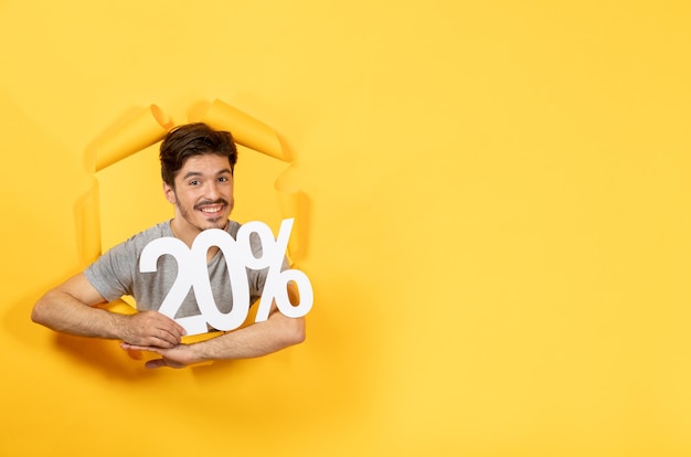 Foto gratuita hombre joven con cartel de inscripción en la superficie de papel amarillo rasgado venta chico de compras