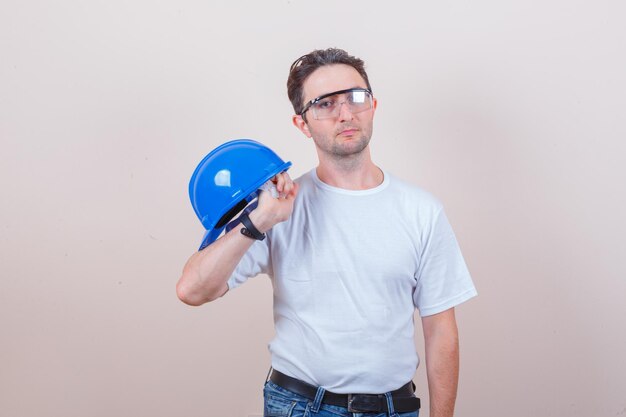 Hombre joven con casco en camiseta, jeans y mirando serio