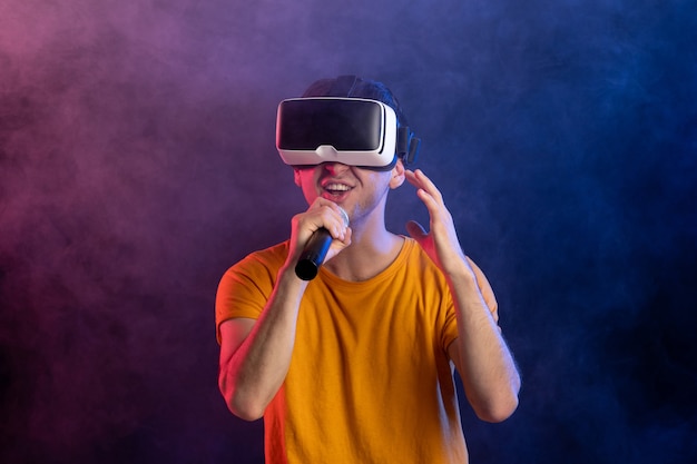 Hombre joven con casco de realidad virtual y sosteniendo micrófono superficie azul oscuro