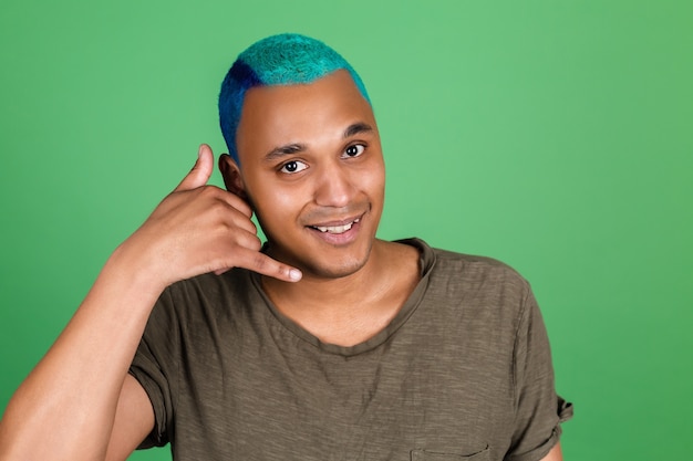 Hombre joven en casual en la pared verde feliz con una sonrisa hace gesto de teléfono