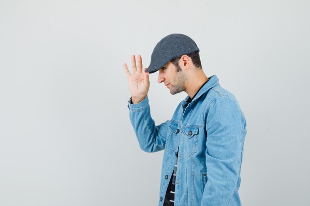 Hombre joven con chaqueta, camiseta tocando su gorra y mirando tranquilo. espacio para texto