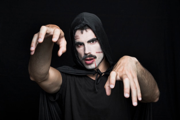 Hombre joven con cicatrices en la cara pálida en traje de Halloween posando en el estudio