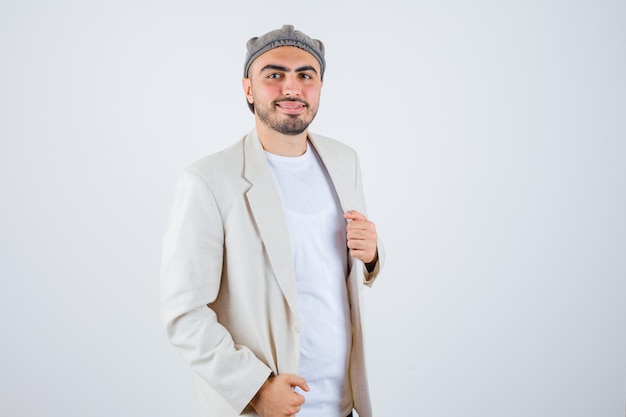 Hombre joven cogidos de la mano en la chaqueta con camiseta blanca, chaqueta y gorra gris y mirando feliz