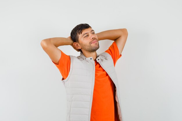 Hombre joven cogidos de la mano detrás de la cabeza en camiseta, chaqueta y mirando relajado. vista frontal.