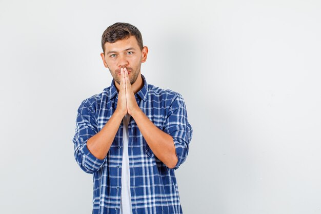 Hombre joven cogidos de la mano en gesto de oración en camisa y mirando alegre. vista frontal.