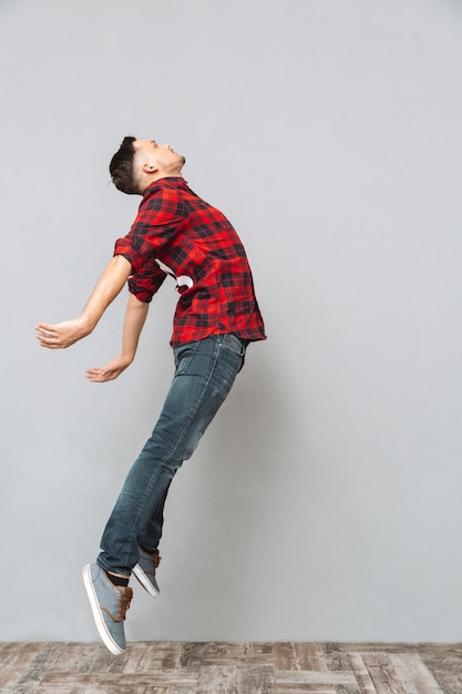 Foto gratuita hombre joven concentrado que salta sobre la pared gris.