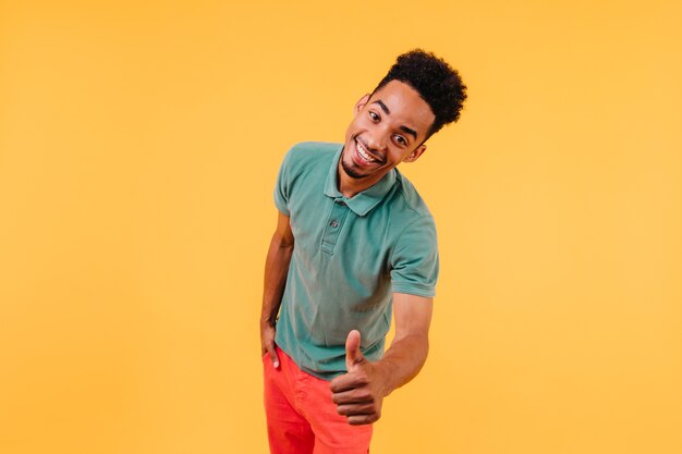 Hombre joven confidente con piel oscura posando con el pulgar hacia arriba. Retrato de feliz chico africano aislado.