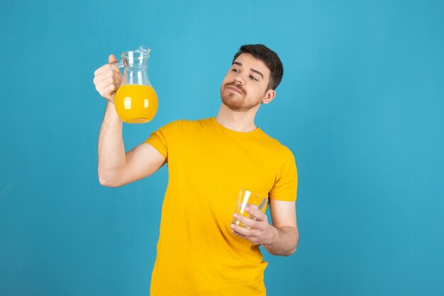 Hombre joven confidente que sostiene la jarra llena con jugo de naranja natural y mirándolo.