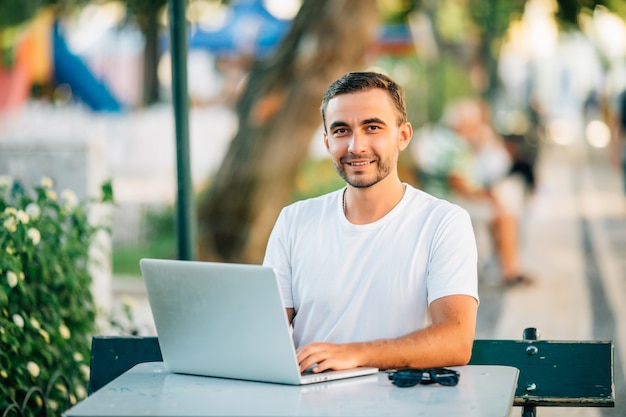 Hombre joven confidente que trabaja en la computadora portátil mientras está sentado en la mesa de madera al aire libre