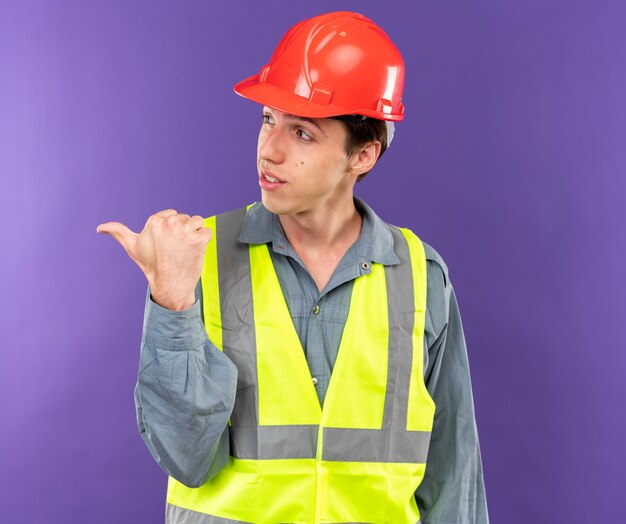 Hombre joven constructor de lado mirando complacido en puntos uniformes al lado