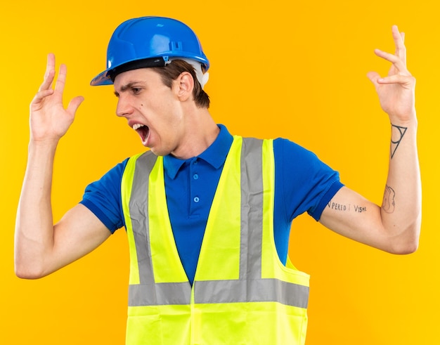 Hombre joven constructor de lado mirando molesto en uniforme extendiendo las manos