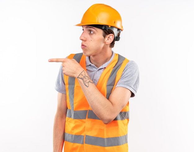 Hombre joven constructor de lado mirando sorprendido en puntos uniformes al lado