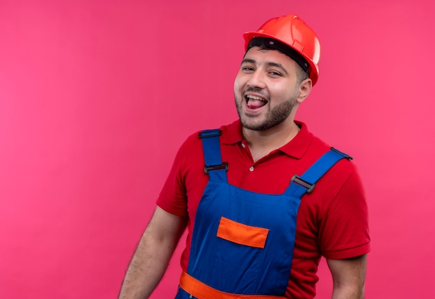 Foto gratuita hombre joven constructor en uniforme de construcción y casco de seguridad sonriendo alegremente sacando la lengua