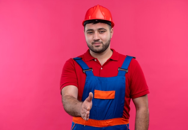 Hombre joven constructor en uniforme de construcción y saludo de casco de seguridad con alguien que ofrece la mano