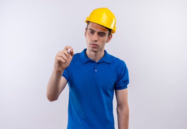 Hombre joven constructor vestido con uniforme de construcción y casco de seguridad escribe con un bolígrafo