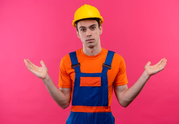 Hombre joven constructor vestido con uniforme de construcción y casco de seguridad está confundido