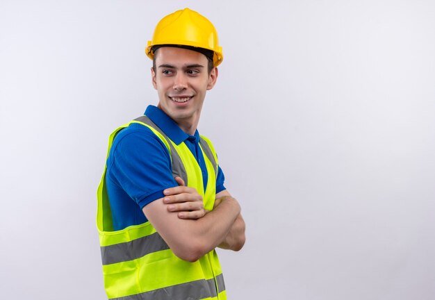 Hombre joven constructor vestido con uniforme de construcción y casco de seguridad felizmente mira hacia los lados