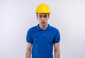 Foto gratuita hombre joven constructor vestido con uniforme de construcción y casco de seguridad haciendo cara de sorpresa