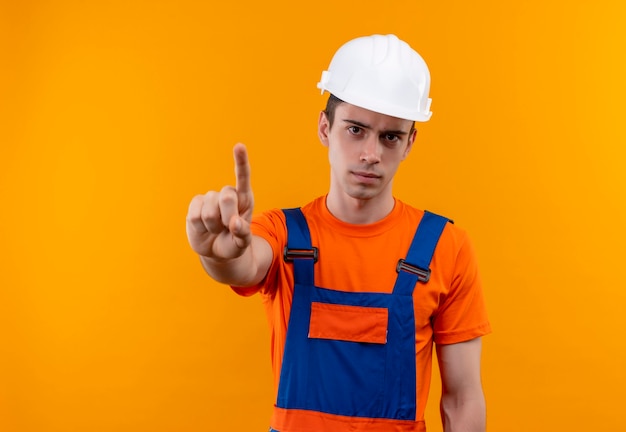 Hombre joven constructor vestido con uniforme de construcción y casco de seguridad haciendo dedo hacia arriba