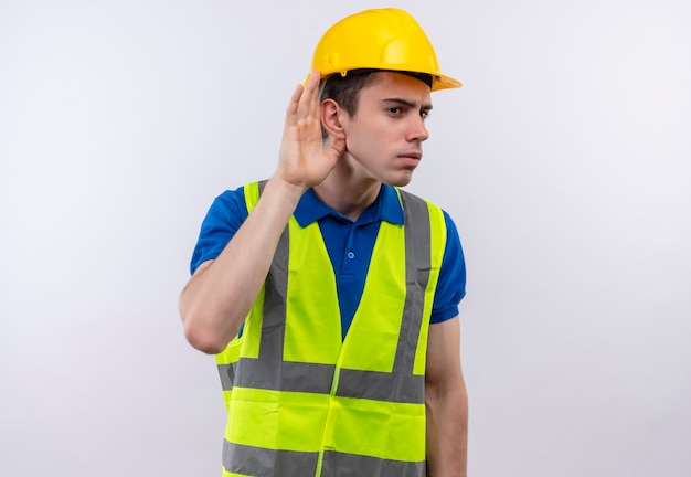 Hombre joven constructor vestido con uniforme de construcción y casco de seguridad intenta escuchar