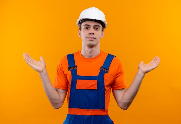 Hombre joven constructor vestido con uniforme de construcción y casco de seguridad levanta las manos