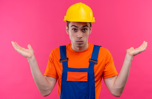 Hombre joven constructor vestido con uniforme de construcción y casco de seguridad no sabe qué hacer