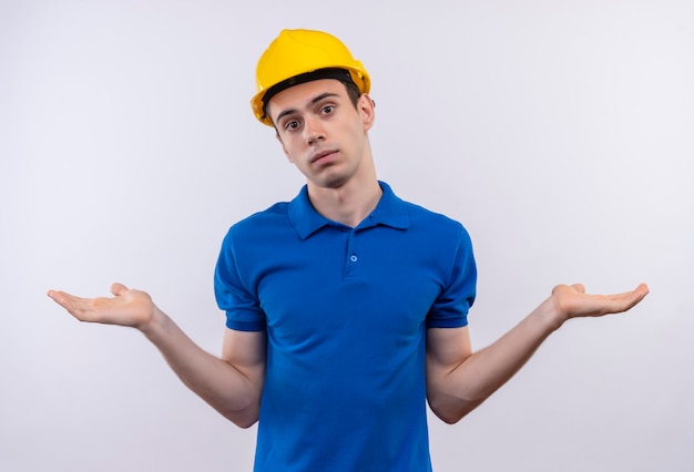 Hombre joven constructor vestido con uniforme de construcción y casco de seguridad no sabe qué hacer