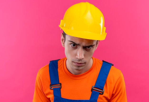 Hombre joven constructor vestido con uniforme de construcción y casco de seguridad pensativo