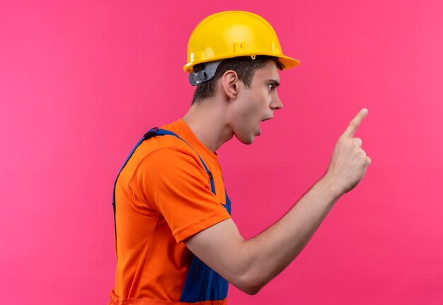 Hombre joven constructor vestido con uniforme de construcción y casco de seguridad regaña a alguien