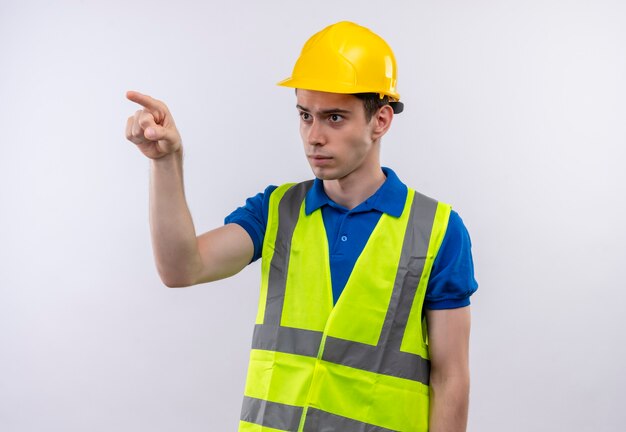 Hombre joven constructor vestido con uniforme de construcción y casco de seguridad señala con el dedo