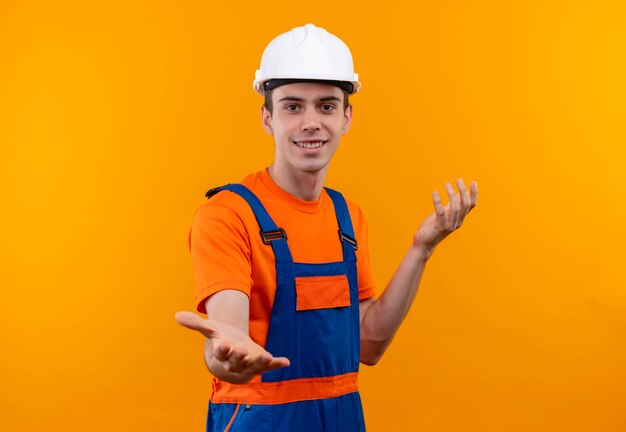 Hombre joven constructor vestido con uniforme de construcción y casco de seguridad sonríe e introduce algo