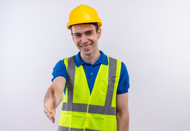 Hombre joven constructor vestido con uniforme de construcción y casco de seguridad sonríe y saluda